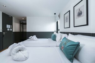Una habitación de hotel con dos camas, ropa de cama blanca, almohadas color turquesa y cuadros en la pared.