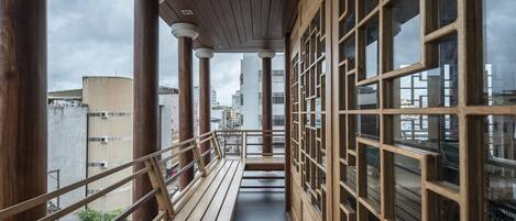 Een gang met houten zuilen en grote ramen, die uitkomt op een balkon met uitzicht op de stadsgezicht.