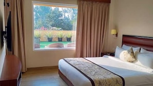Habitación de hotel con una cama grande, televisión, piso de madera y ventana con cortinas.