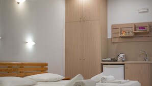 A bedroom with a wooden bed, a small bedside table, a built-in wardrobe, and a kitchenette area with a sink and a kettle. - Stefania Studios Stalis (Hersonissos)