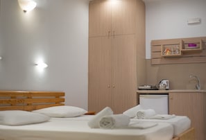 A bedroom with a wooden bed, a small bedside table, a built-in wardrobe, and a kitchenette area with a sink and a kettle. - Stefania Studios Stalis (Hersonissos)