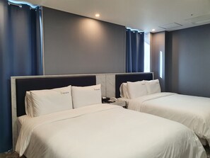 A hotel room with two beds, each with white bedding and headboards, and a nightstand with a phone.