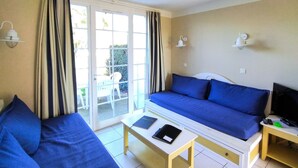 Una habitació amb un sofà blau, una taula petita amb un llibre i un comandament, i una televisió sobre un suport.