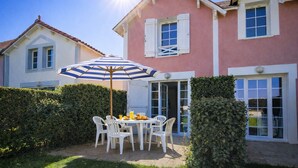 Una casa de dues plantes amb un pati que inclou taula i cadires, i un parasol rayat.