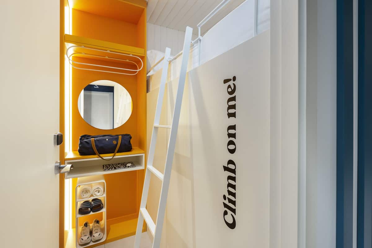A hotel room with a wardrobe containing a hanging bag, a mirror, and a shelf with shoes.
