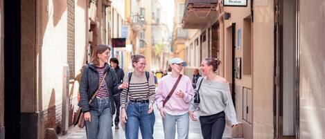 Una calle estrecha con edificios a ambos lados, un letrero que dice 'Coo Beatas' y un grupo de personas caminando.