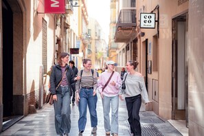 A narrow street with buildings on either side, a sign for 'Coo Beatas,' and a group of people walking. -  Coeo Pod Hostel Beatas (Málaga)