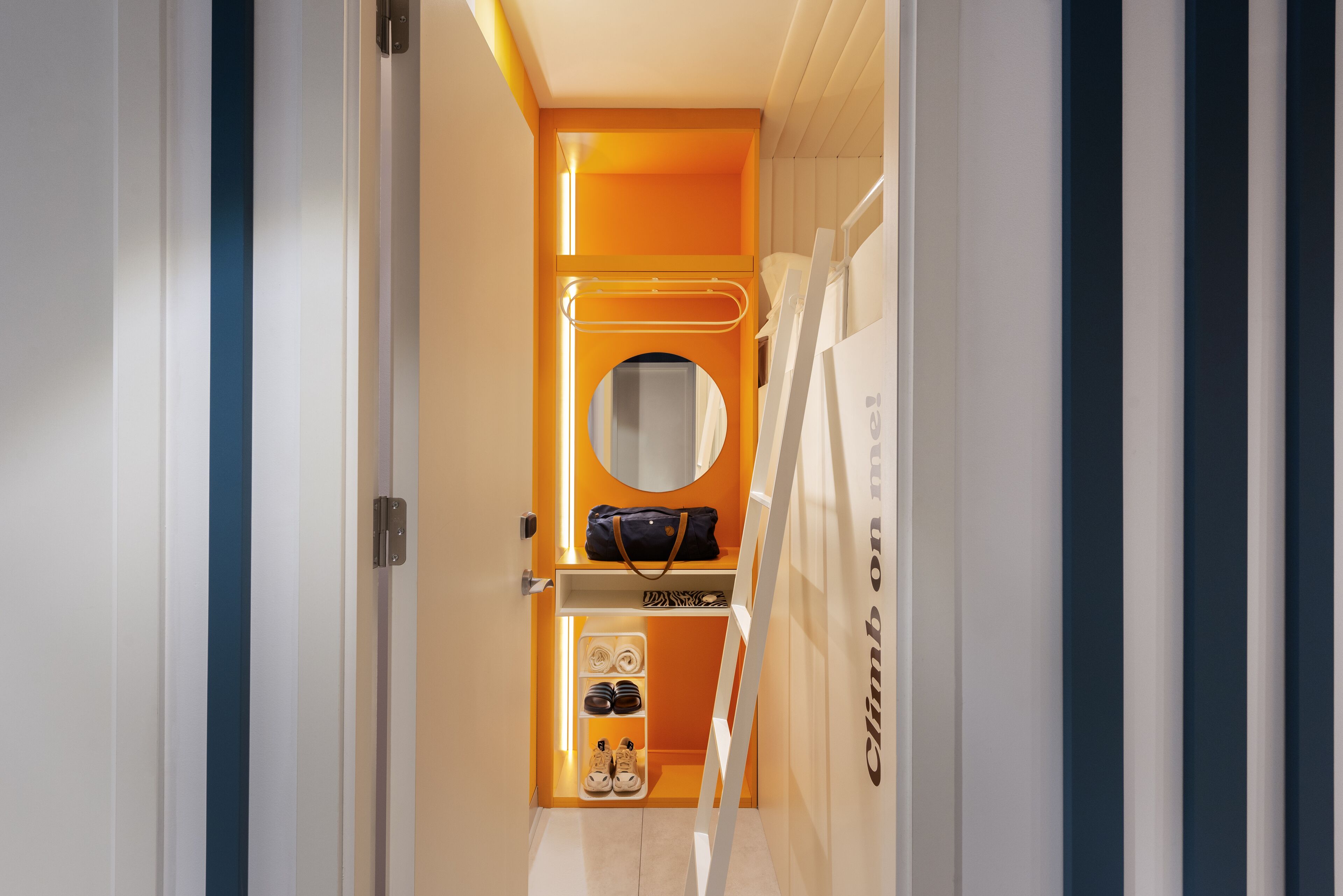 Ein schmaler Flur mit einer orangefarbenen Akzentwand, einem runden Spiegel und einem Schuhregal.
