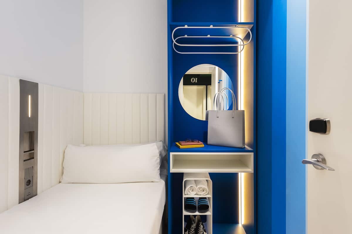 A modern hotel room with a bed, a built-in wardrobe, a mirror, and a shoe storage unit.