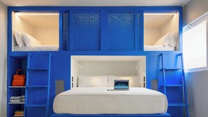 A bunk bed with a laptop on the lower bunk, a blue wardrobe, and a shelf with books and a handbag. - Coeo Pod Hostel Beatas (Málaga)