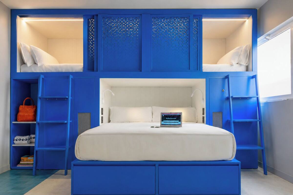 A bunk bed with a laptop on the lower bunk, a blue wardrobe, and a shelf with books and a handbag.