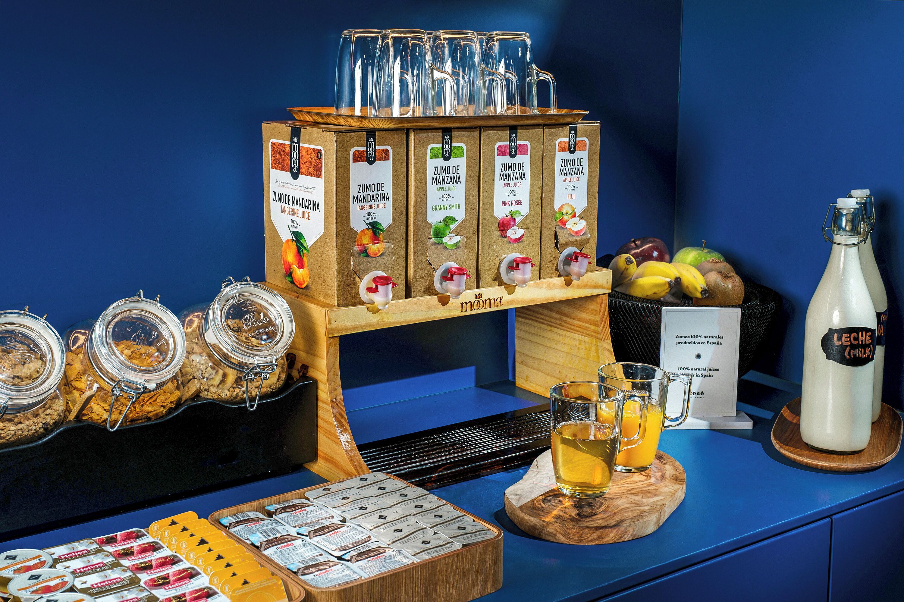 Un bufé de desayuno con diversas opciones de comida, un dispensador de leche y una selección de frutas.