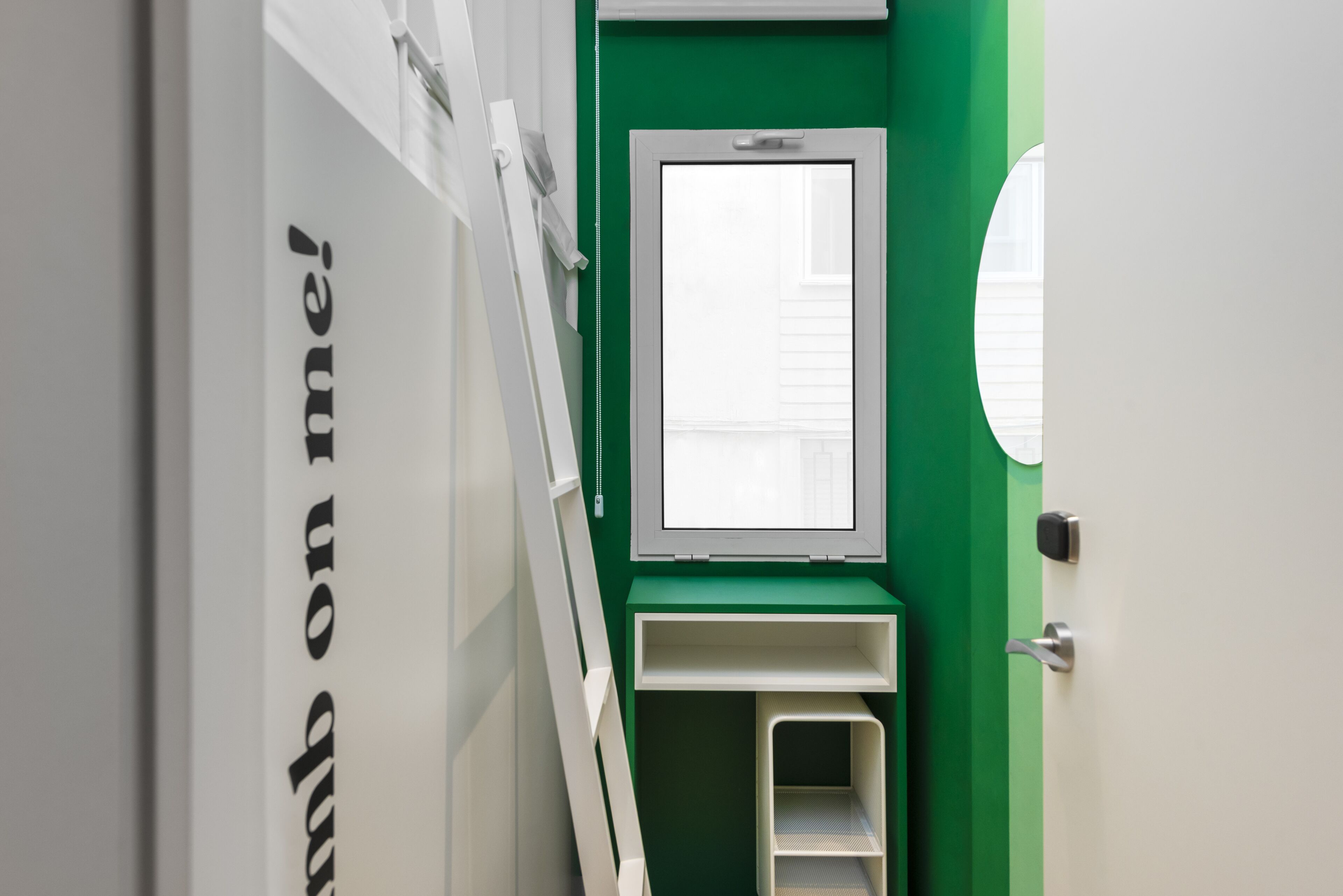 Un pasillo estrecho con una pared verde, una puerta blanca y una ventana con persianas.
