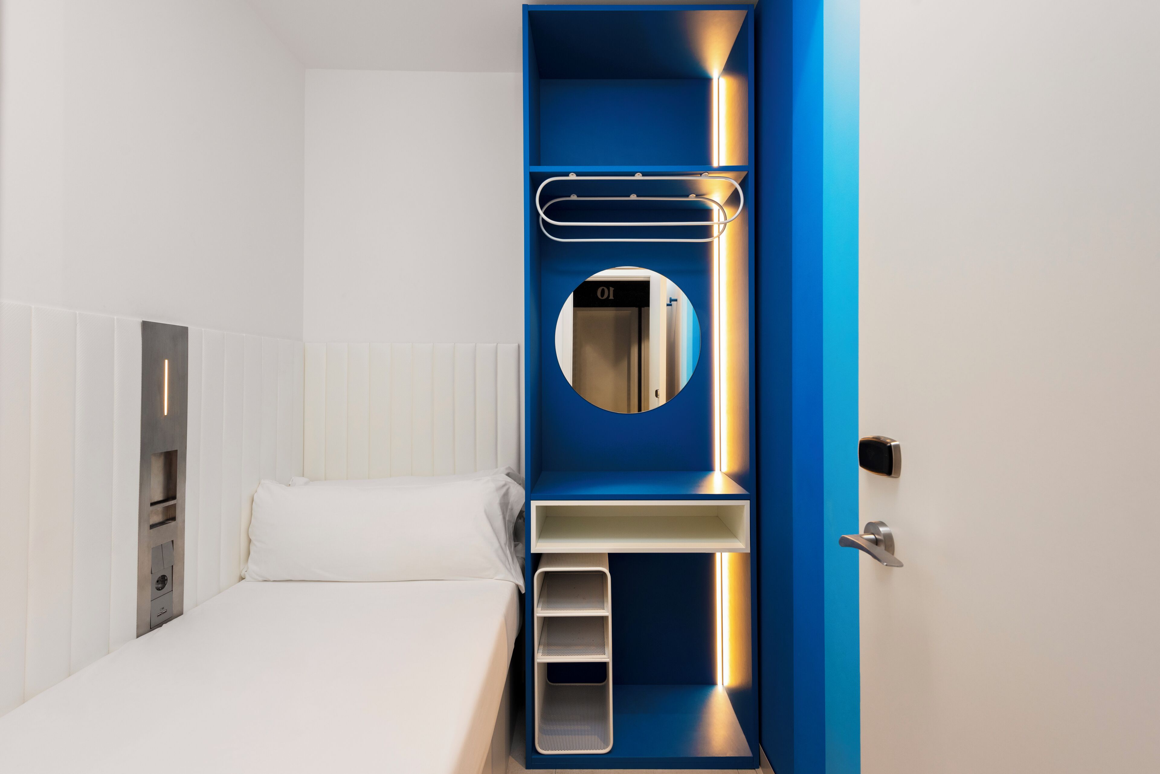 A modern hotel room with a bed, a built-in wardrobe with a mirror, and a small seating area.