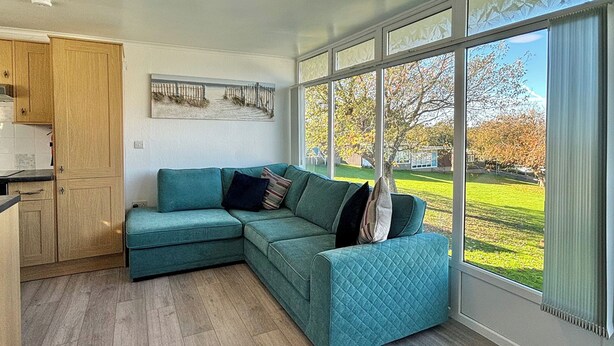 Uma sala de estar moderna com um sofá seccional verde-água, um armário de madeira e uma grande janela com vista para um gramado verde.