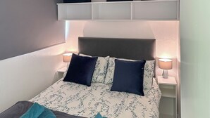 Cama bem arrumada com colcha florida, dois travesseiros e duas toalhas verde-água.