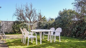 Une terrasse avec une table ronde et quatre chaises, entourée d’une pelouse verdoyante et d’une clôture en bois.