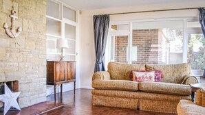 Un salon avec un canapé à motifs, une décoration en forme d’étoile au mur, un meuble en bois et une grande fenêtre avec des rideaux.