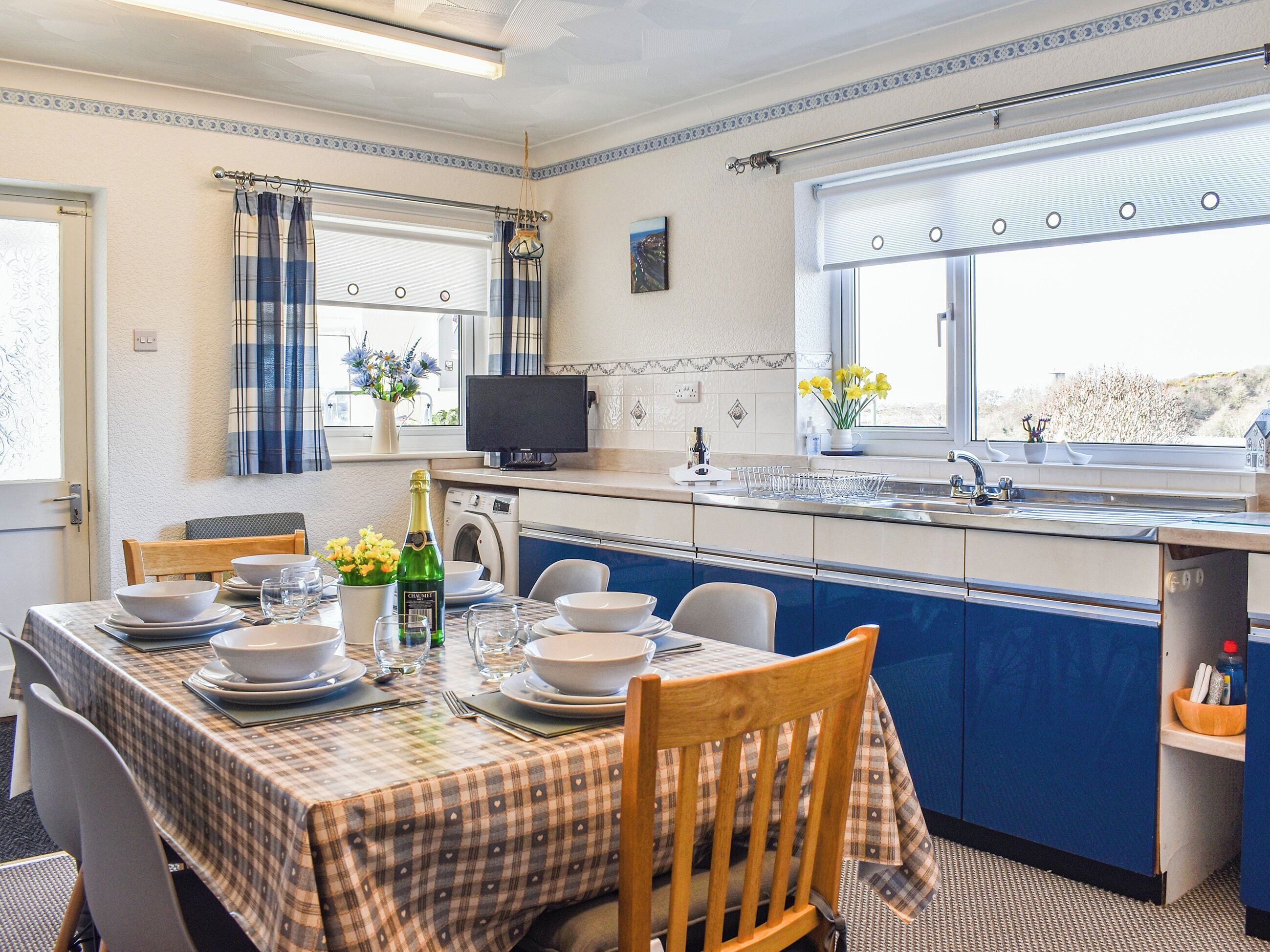A compact kitchen with a dining area, a washing machine, and a window with curtains.