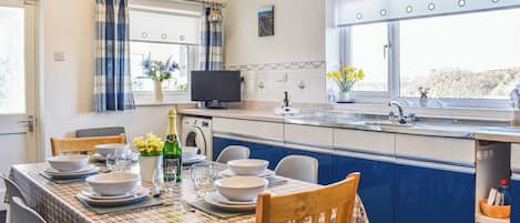 Cocina compacta con comedor, lavadora y ventana con cortinas.