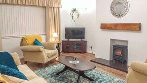 Un salón con sofá, sillón, mesa de centro, televisor, aparador, chimenea y espejo decorativo.