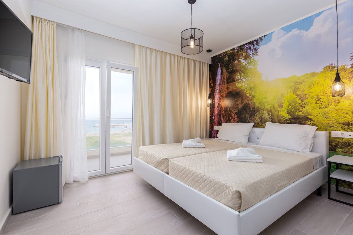 Quarto de hotel com cama grande, televisão fixada na parede e um mural com paisagem.