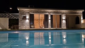 Una casa moderna con piscina, fachada de piedra y amplios ventanales correderos.