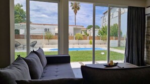 Una sala de estar moderna con un gran ventanal corredero que da a un patio trasero con piscina y vistas a casas vecinas.