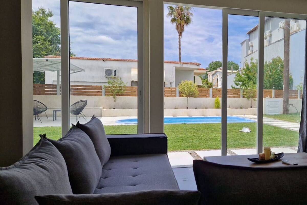 Sala de estar moderna com uma grande porta de vidro deslizante que dá para um quintal com piscina e vista para as casas vizinhas.