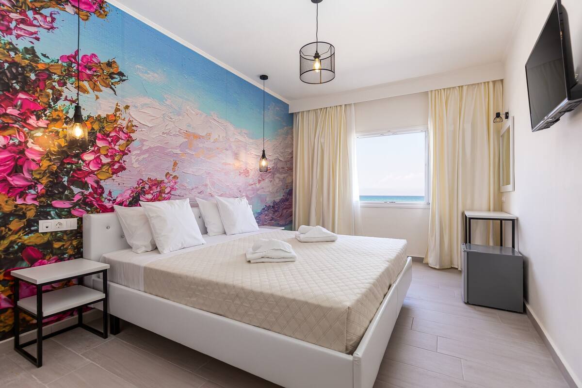 Quarto bem arrumado com cama, mesa de cabeceira e um mural na parede.