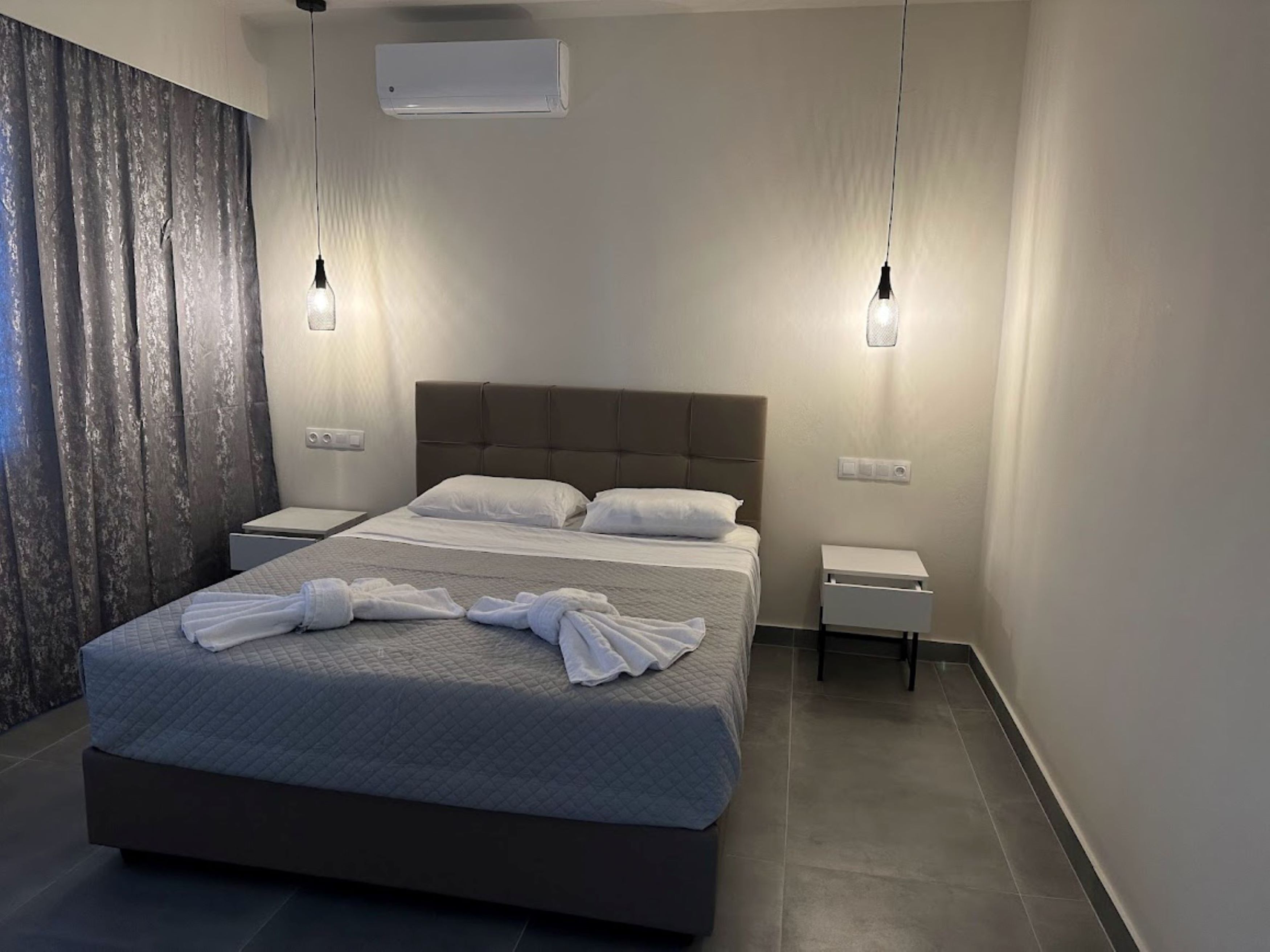 A modern hotel room with a large bed, two bedside tables, and a wall-mounted air conditioner.