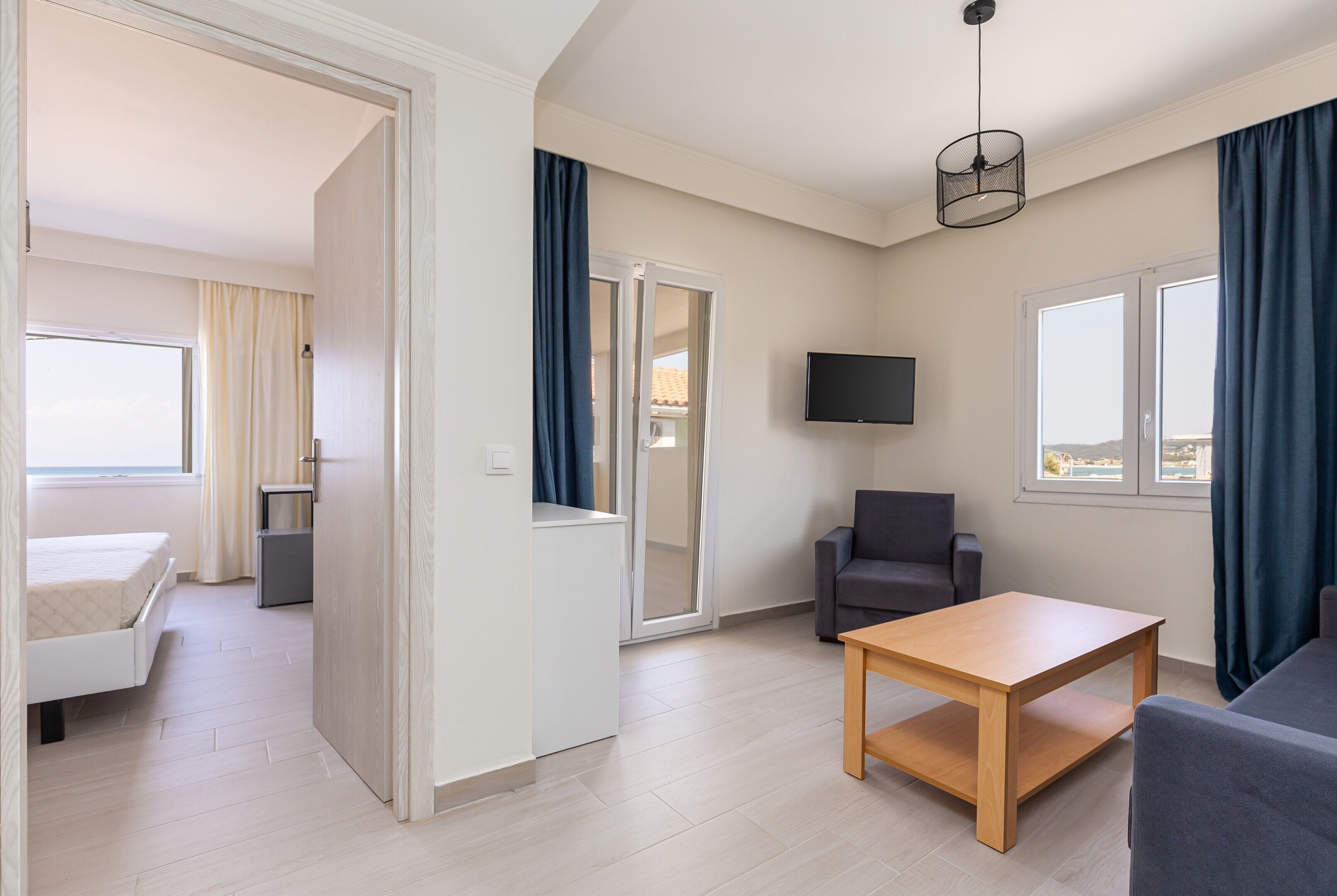 A modern hotel room with a bed, a desk, a chair, a TV, and a view of the outdoors.