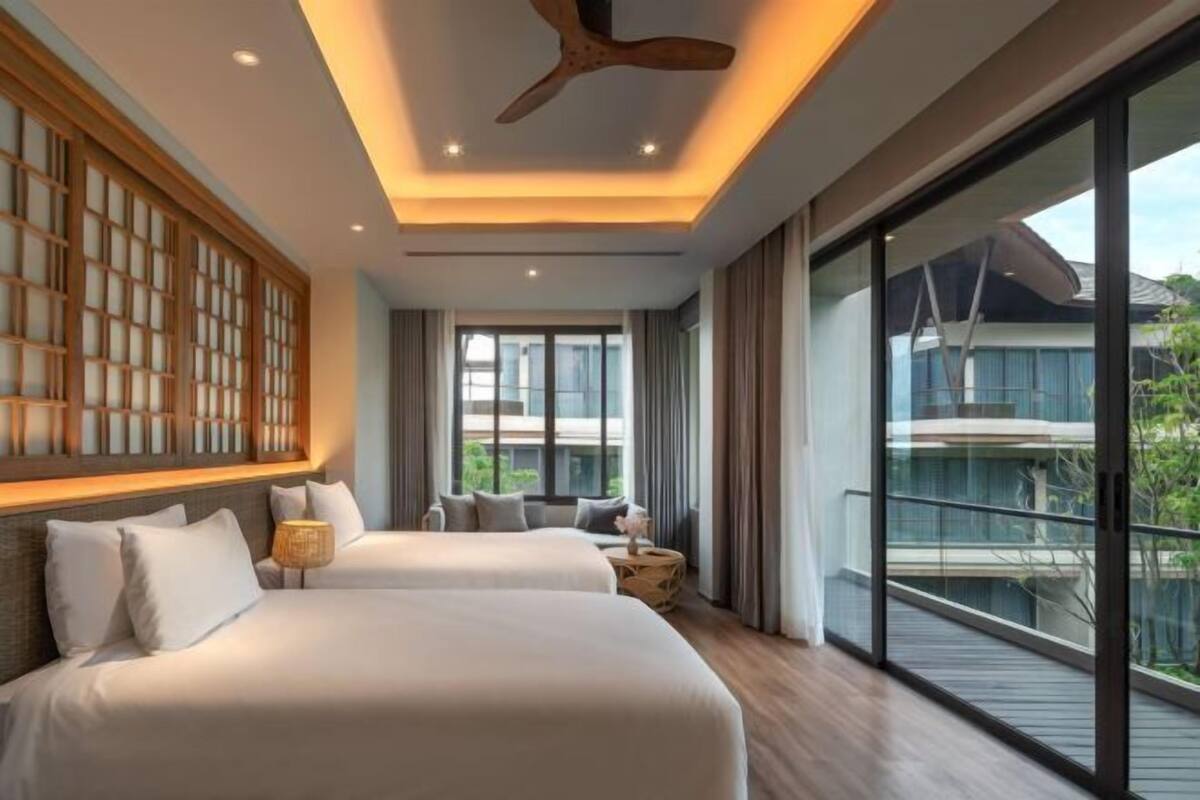 A modern hotel room with two beds, a ceiling fan, large windows, and a balcony with a view.