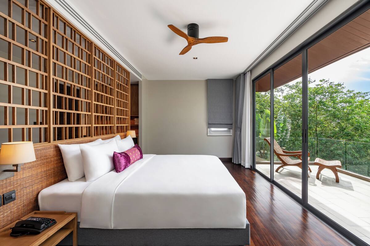 A modern hotel room with a large bed, wooden headboard, and a balcony with outdoor furniture.