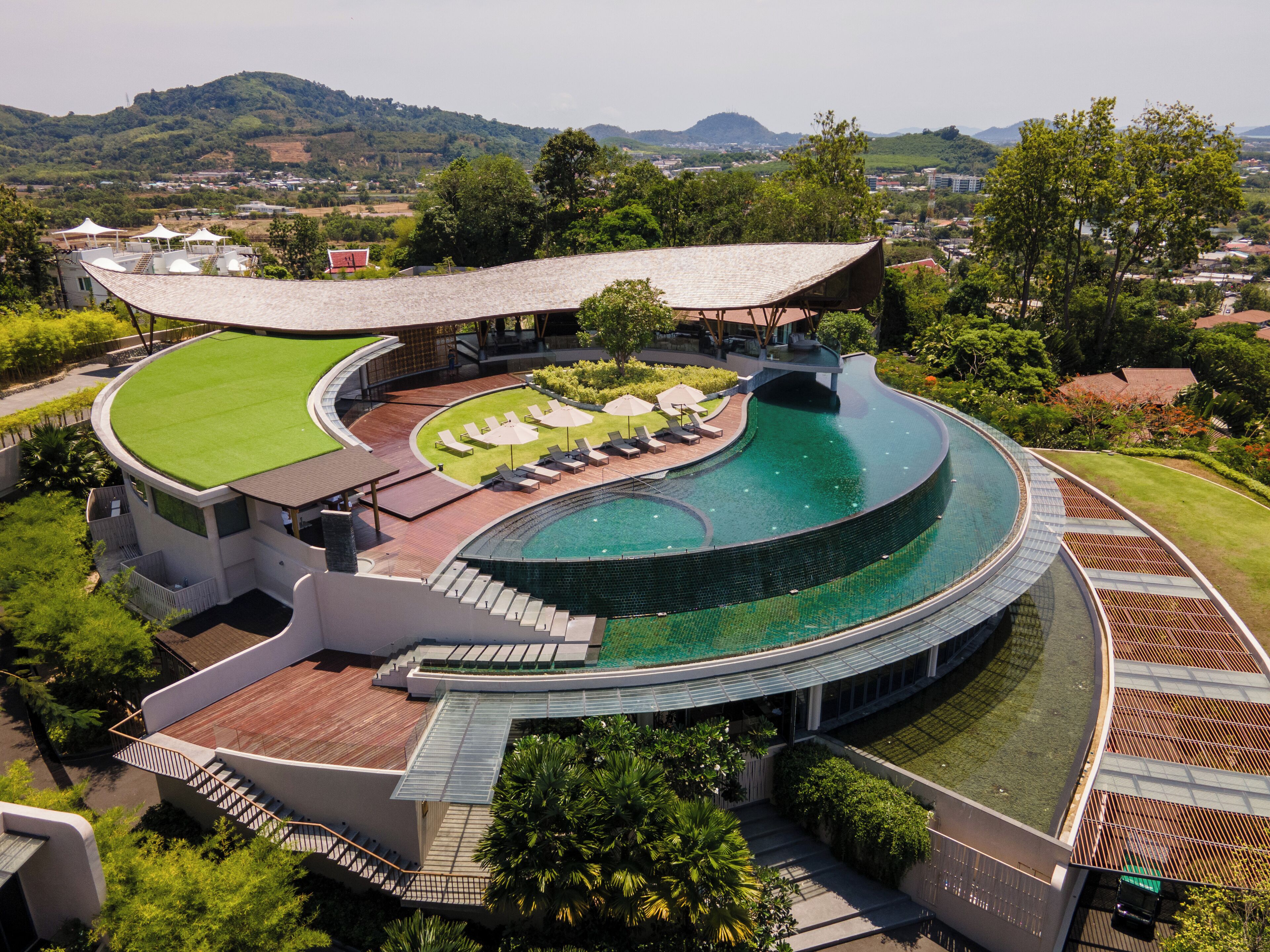A modern resort with a large swimming pool, outdoor lounge area, and a view of the surrounding landscape.