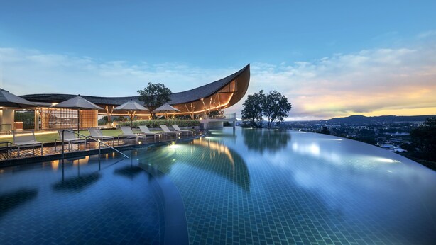 Un hotel moderno con piscina a forma curva e area relax, immerso in un panorama urbano.