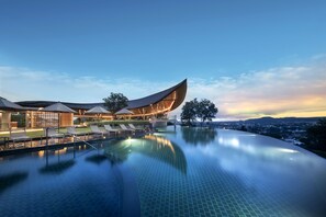 A modern hotel with a curved pool and lounge area, surrounded by a cityscape. - Noku Phuket (Chalong)