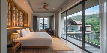 A modern hotel room with a large bed, a ceiling fan, a view of a balcony, and a large window.