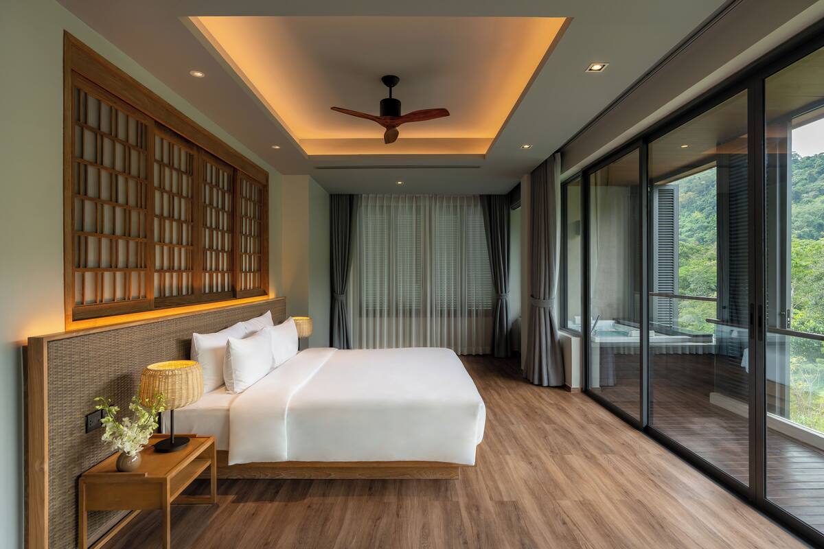 A modern bedroom with a large bed, wooden headboard, and a view of a balcony.