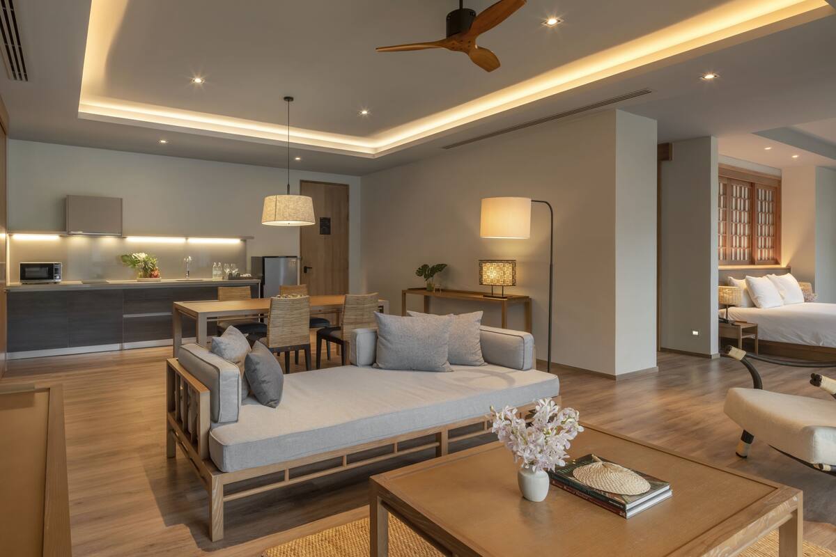 A modern hotel room with a sofa, a dining area, a kitchen, and a bedroom.