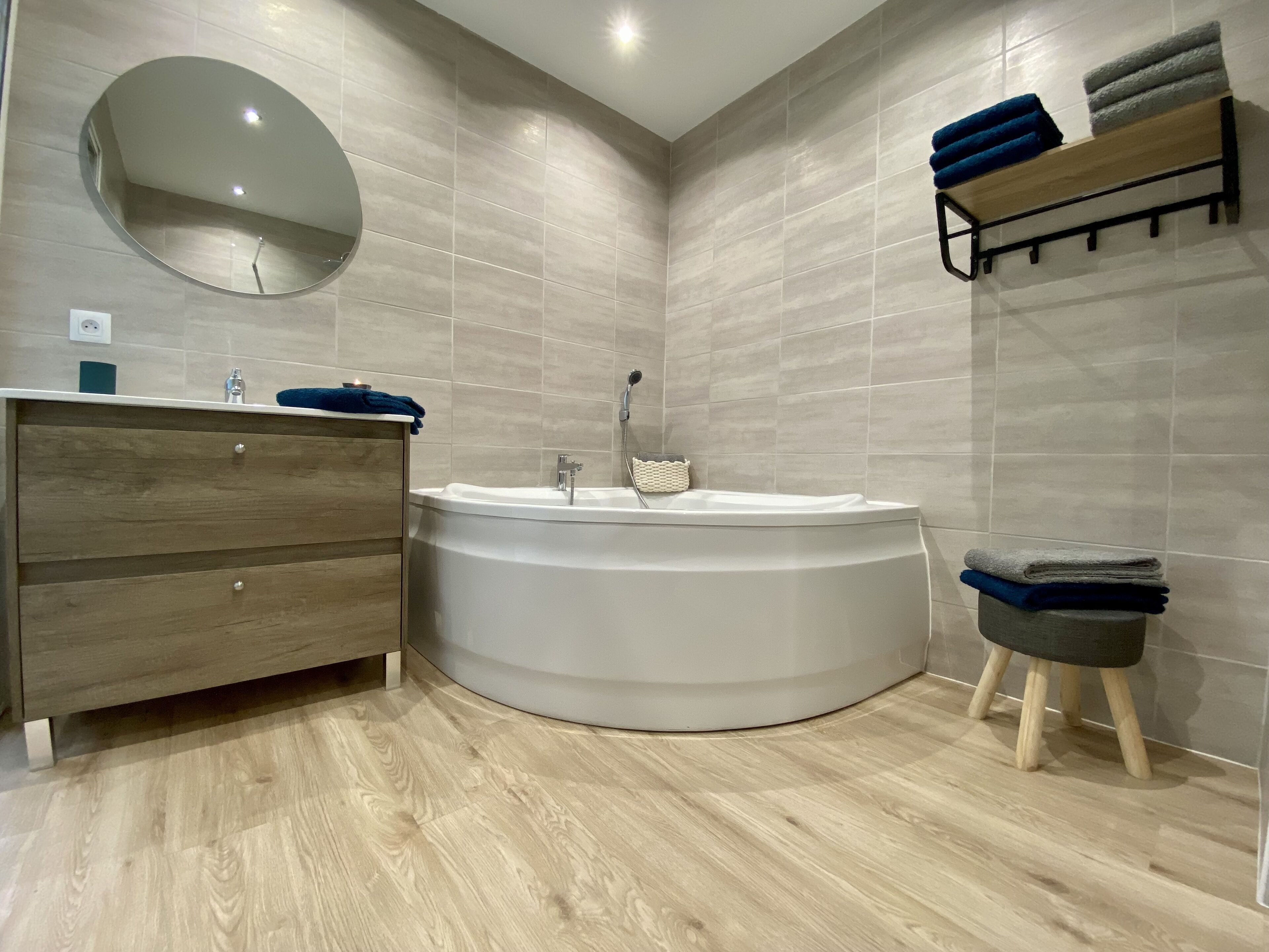 A modern bathroom with a freestanding bathtub, a wooden vanity, a round mirror, and a towel rack.
