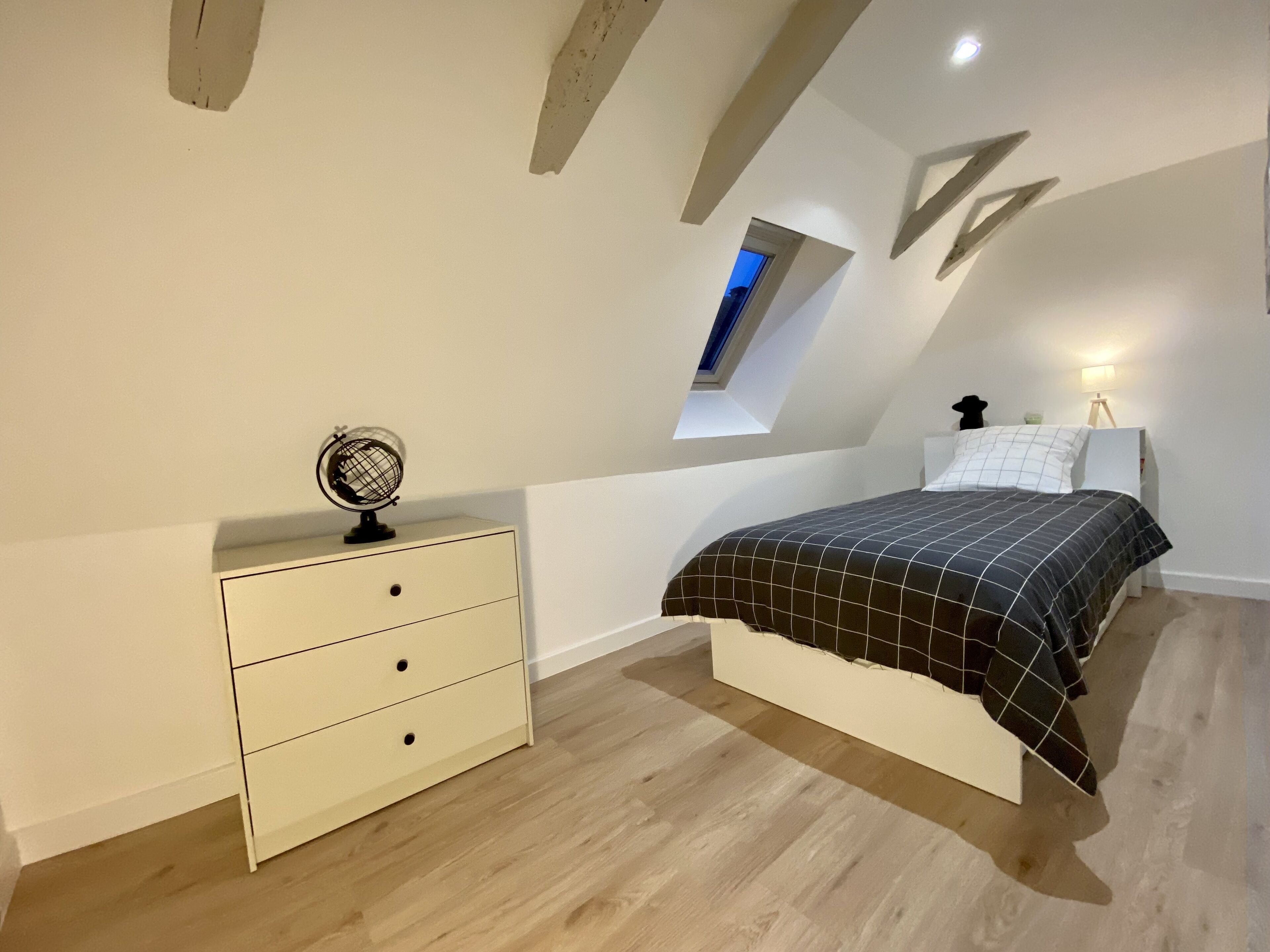 A bedroom with a bed, a nightstand, a dresser, a globe, and a skylight.