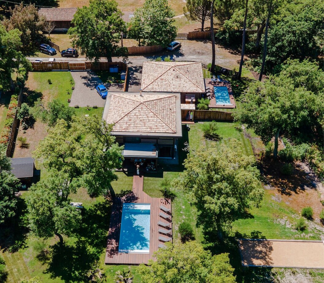 Ein modernes Haus mit zwei großen Schwimmbecken, umgeben von üppiger Vegetation und einem eingezäunten Garten.