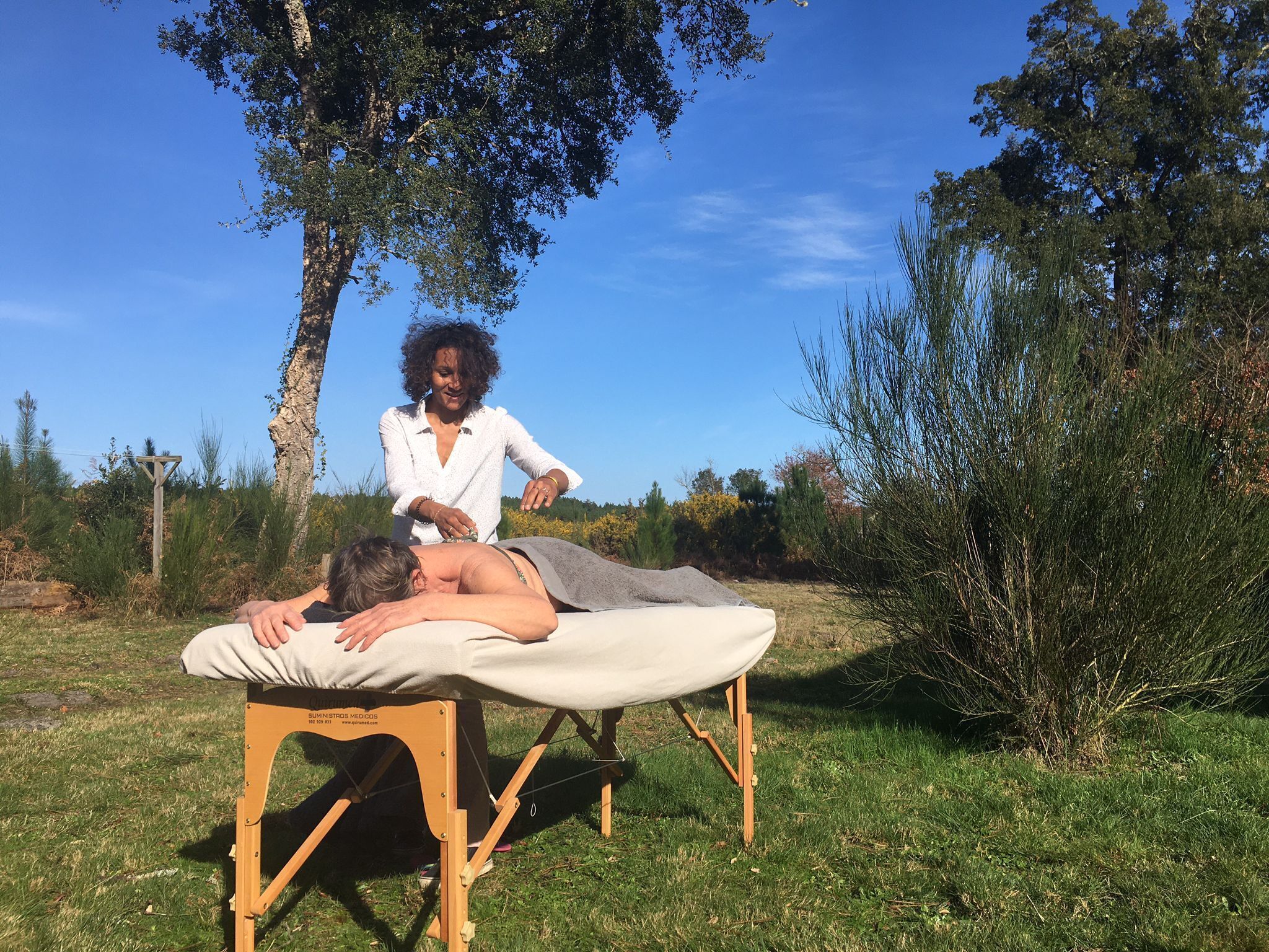 Eine Person liegt auf einer Massageliege im Freien, während ein Therapeut daneben steht.