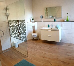 Un baño moderno con cabina de ducha de vidrio, inodoro y tocador blancos, y piso de madera.