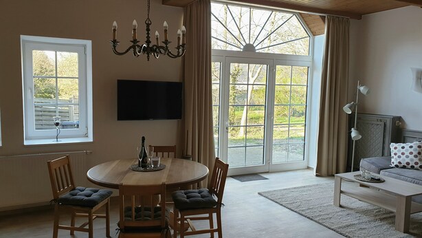 Ein Essbereich mit einem runden Tisch, Stühlen, einer Chandelier und einem an der Wand montierten Fernseher.