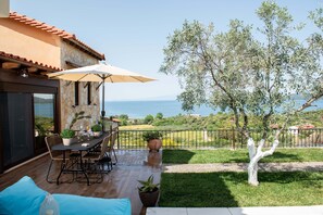 Eine Terrassensitzgelegenheit im Freien mit Tisch, Stühlen und einem großen Sonnenschirm, mit Blick auf das Meer.