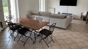 A modern living room with a dining area, a sofa, and a flat-screen TV mounted on the wall. - SPACIOUS APARTMENT CLOSE TO ALL AMENITIES (CONTES)