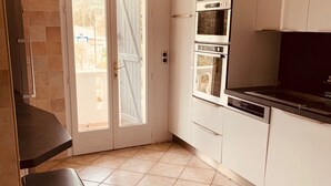 A kitchen with white cabinets, a black countertop, and a double door leading outside. - SPACIOUS APARTMENT CLOSE TO ALL AMENITIES (CONTES)