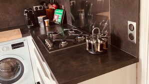A compact kitchen with a stove, a washing machine, and a coffee maker. - SPACIOUS APARTMENT CLOSE TO ALL AMENITIES (CONTES)